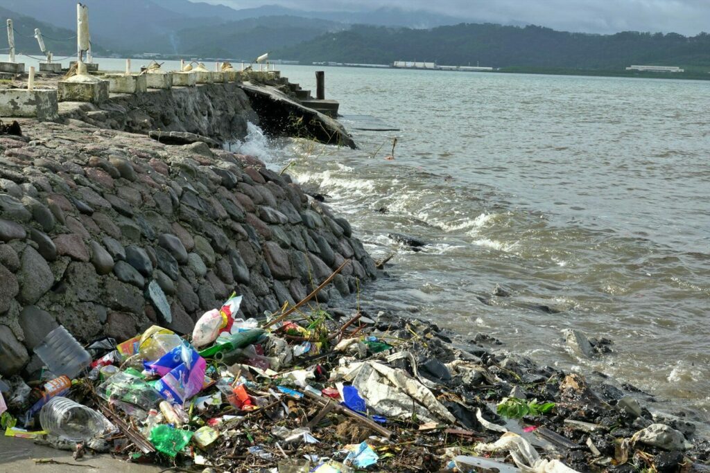 Trash litters the shoreline next to a stone wall.